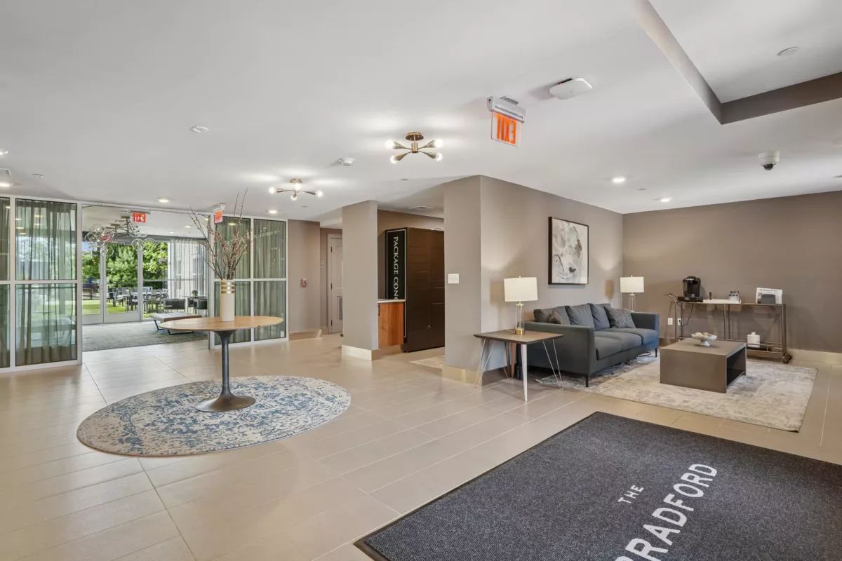 Lobby with round table, blue rug, and glass wall overlooking green courtyard.