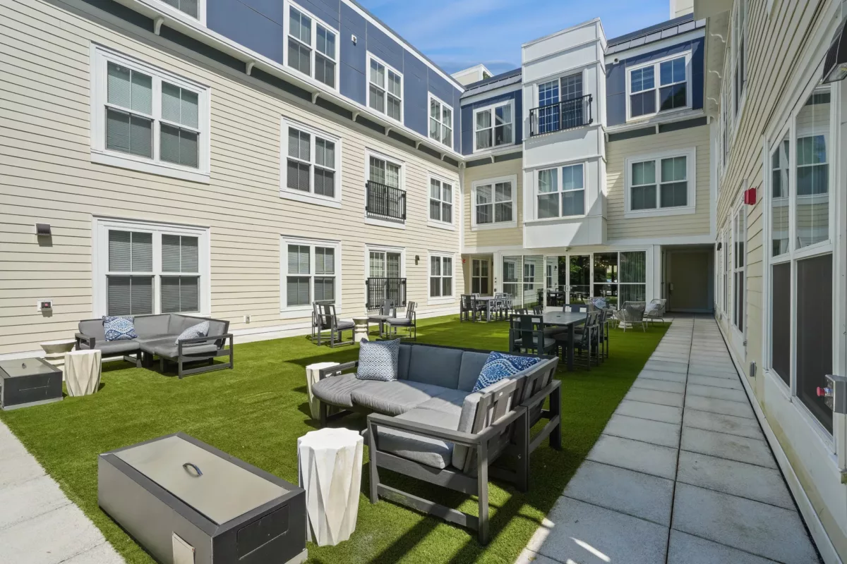 Courtyard with gray sectional seating, dining tables, and artificial grass.