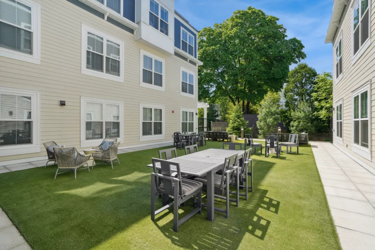 Outdoor courtyard with black dining tables, wicker chairs, and artificial grass.