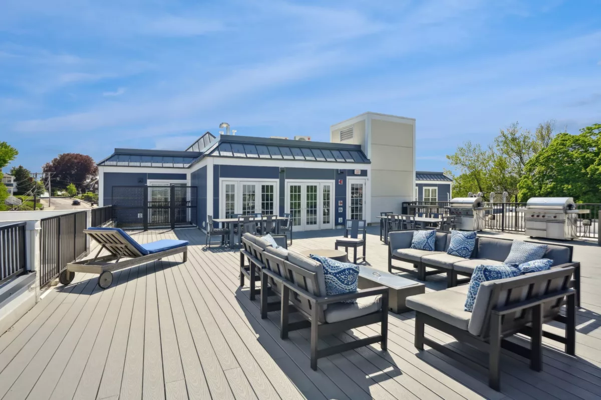 Modern rooftop lounge with blue cushioned chairs, grills, and French doors.