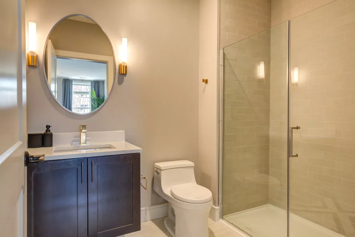 Master bathroom at The Bradford, with dark vanity cabinets, mirror and sconces, and frameless shower