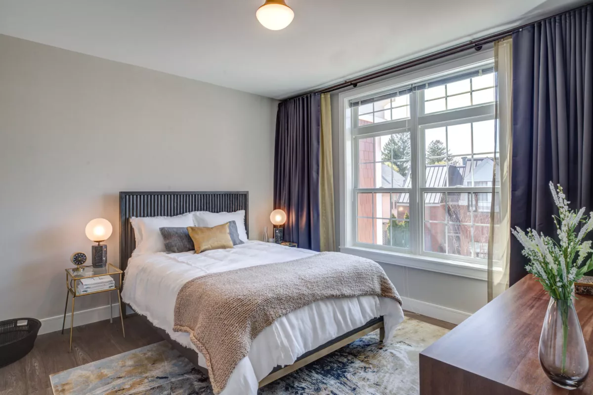 Apartment bedroom with large window, curtains, bed, and furniture at The Bradford
